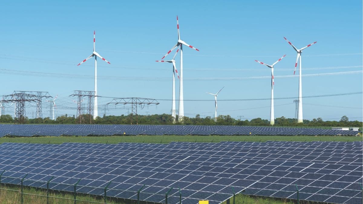 Large solar power plant with rows of photovoltaic panels and wind turbines connected to transmission lines, representing large-scale renewable energy expansion and grid integration.