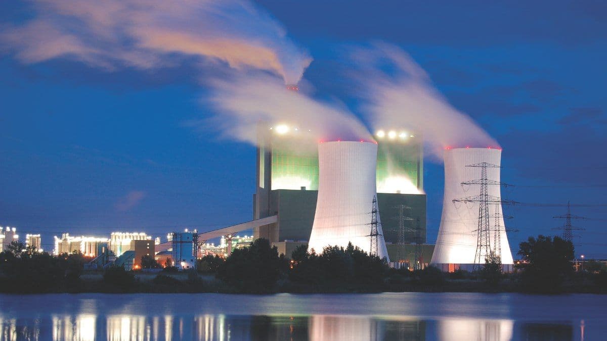 Thermal power plant cooling towers emitting steam with transmission lines at night.