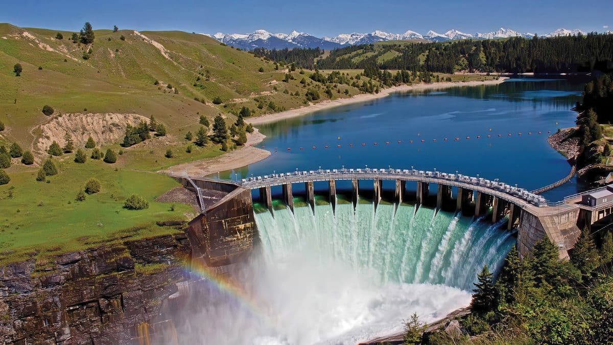Hydroelectric dam releasing water from reservoir surrounded by green hills and mountains.